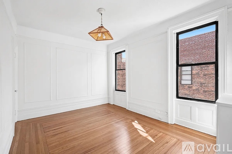 A room with wooden floors and white walls, featuring a hanging light fixture and a window with a brick view.