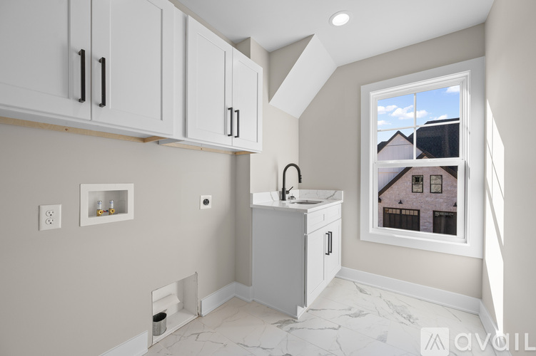 A kitchen with white cabinets and a window showing a house.