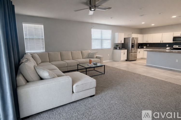 A spacious living room with a grey sofa and a kitchen in the background.