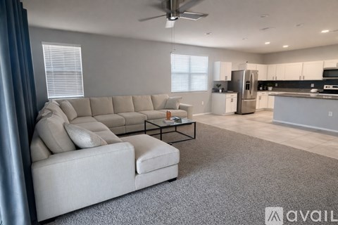 A spacious living room with a grey sofa and a kitchen in the background.