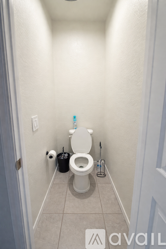 A white toilet in a small bathroom with a trash can and a toilet brush.