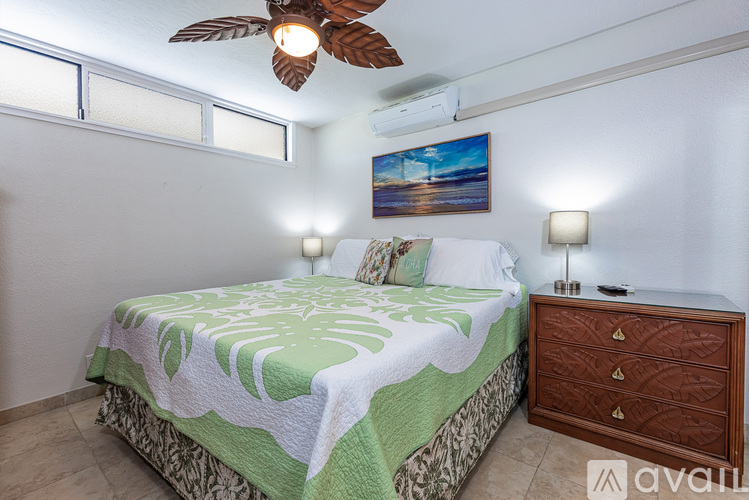 A bedroom with a bed, a ceiling fan, and a painting on the wall.