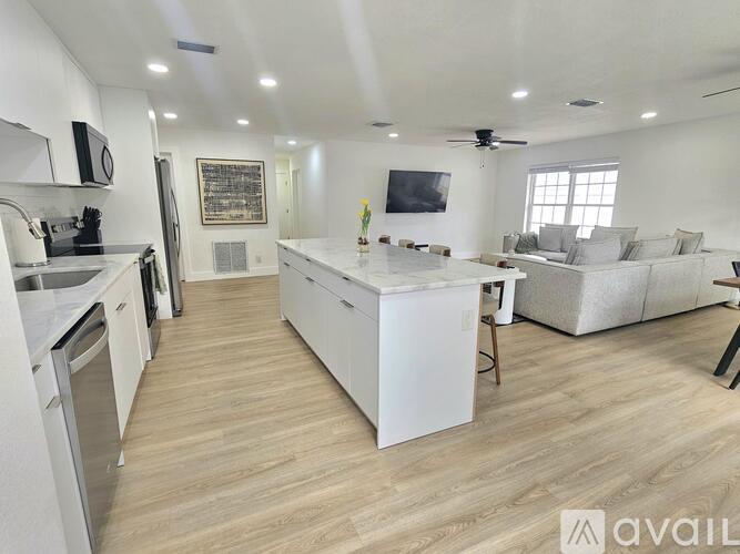 A spacious kitchen and living room with light wood flooring and white appliances.