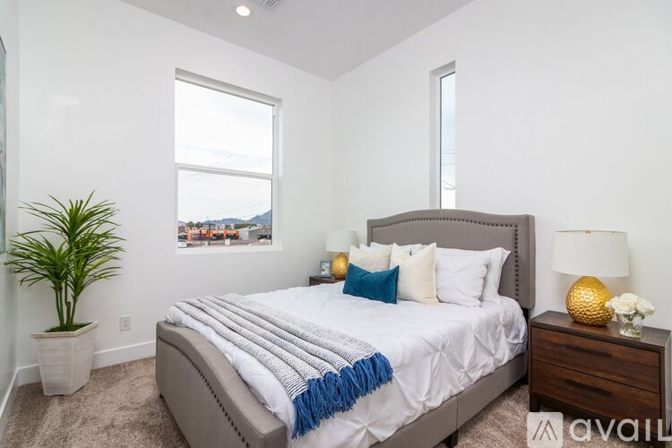 A bedroom with a large bed, a potted plant, and a window with a view of a cityscape.