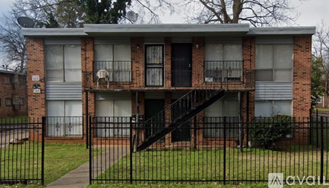 A brick apartment building with a black fence in front.