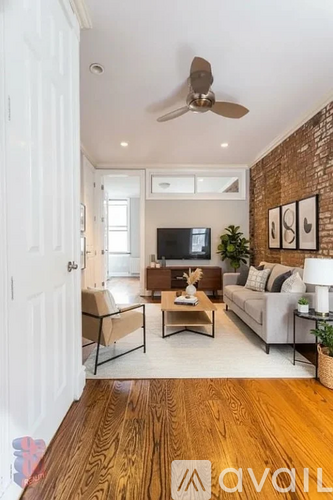 A living room with a white couch, a wooden floor, and a brick wall.