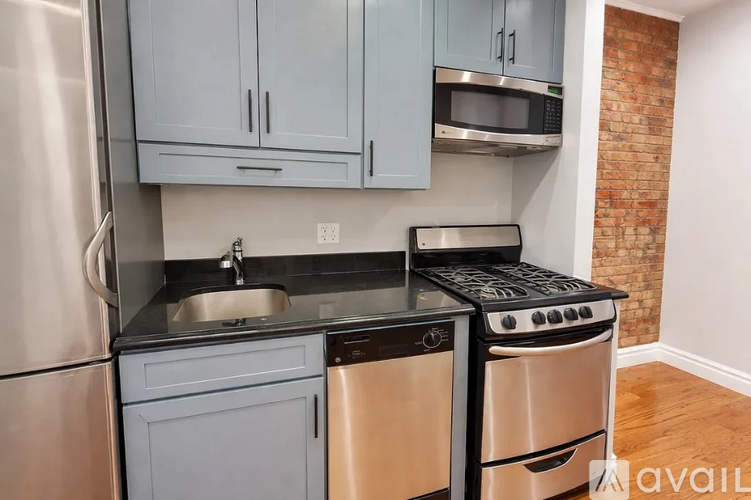 A kitchen with a stainless steel refrigerator, a black countertop, and a brick wall.