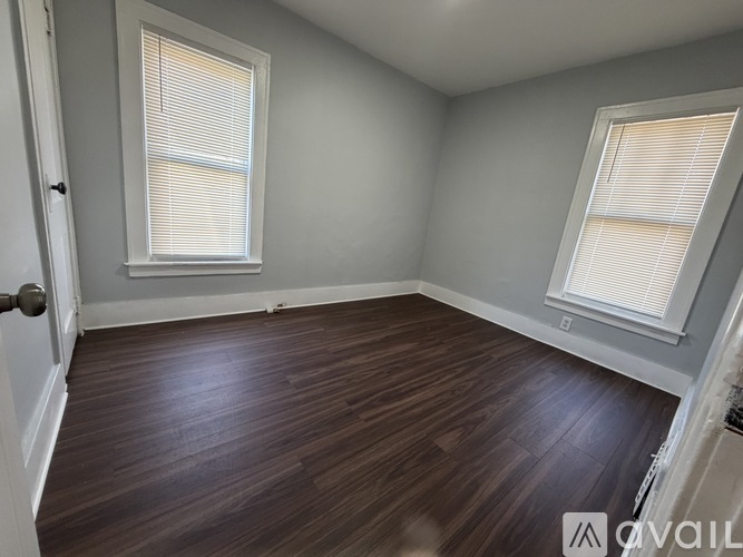 A room with wooden floors and two windows with blinds.