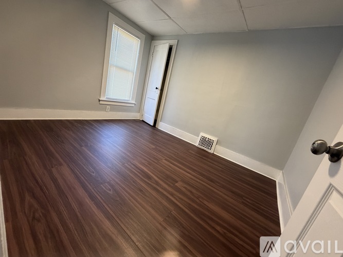 A room with wooden flooring and a door leading to another room.