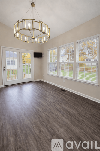 A room with a chandelier, wooden flooring, and a large window with blinds.