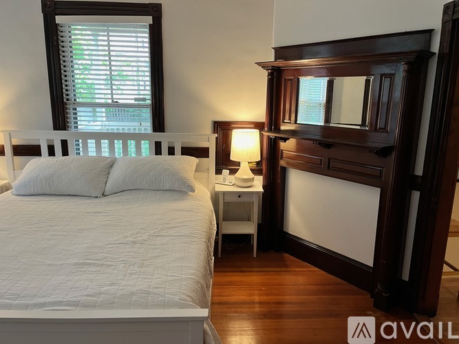 A bedroom with a large bed, a nightstand with a lamp, and a wooden dresser.