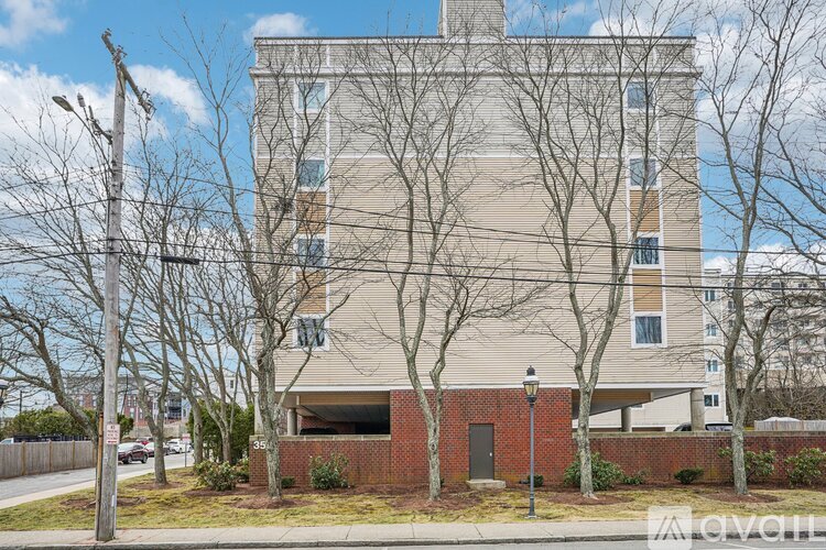 A tall building with a brick base and a grey facade stands between two bare trees.