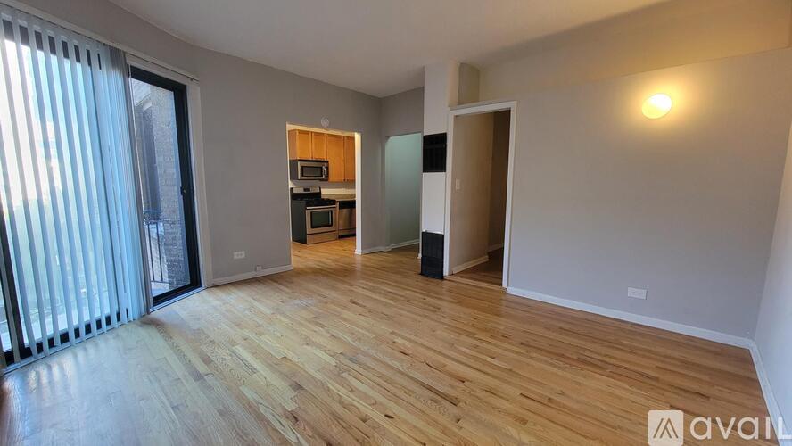A spacious room with wooden flooring and a kitchen area in the background.