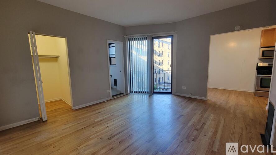 A spacious room with wooden flooring and a large window with blinds.