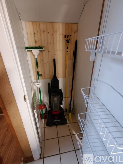 A white fridge in a kitchen with a broom leaning against the wall.