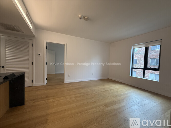A spacious room with wooden flooring and a large window with blinds.