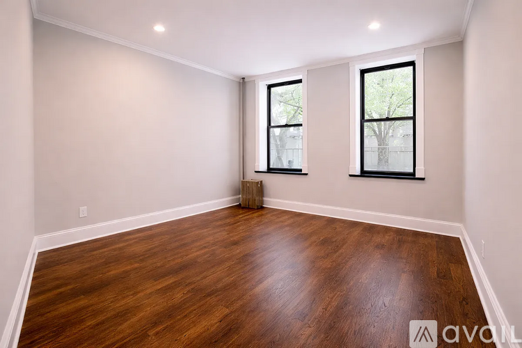 A room with wooden flooring and two windows.