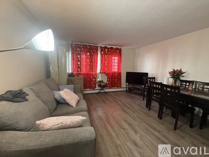 A living room with a grey couch, a wooden dining table, and a red curtain.