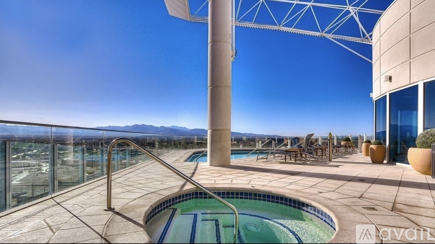 A hot tub is in the middle of a patio with a glass wall behind it.