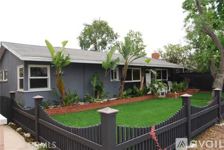 A grey house with a fence and green plants.