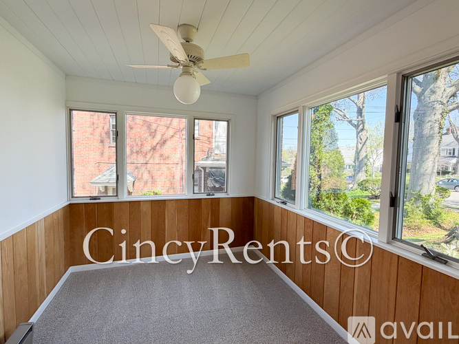 A room with a ceiling fan and large windows overlooking a tree and a building.