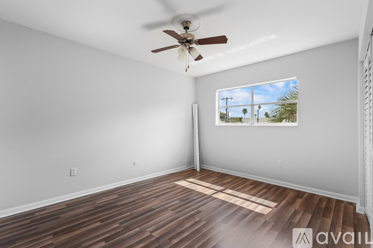 A room with a ceiling fan and a window showing a view of palm trees.