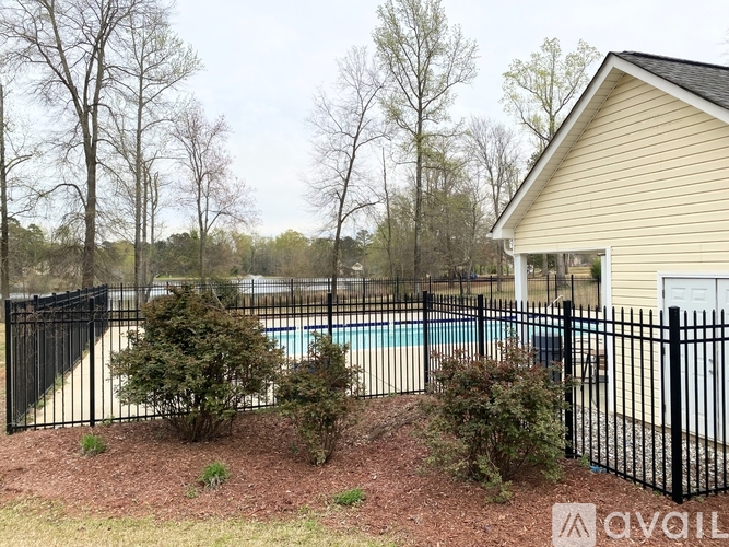 A pool surrounded by a black fence and a house in the background.