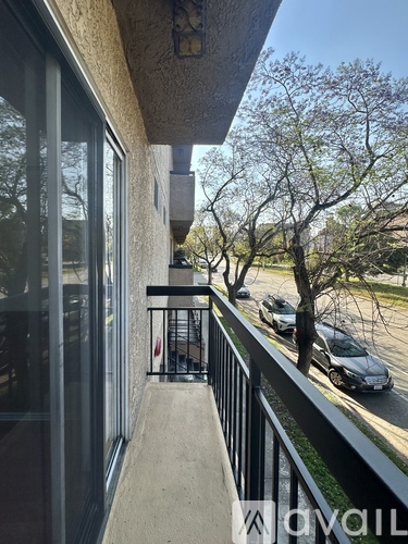 A balcony with a black railing and a view of cars and trees.