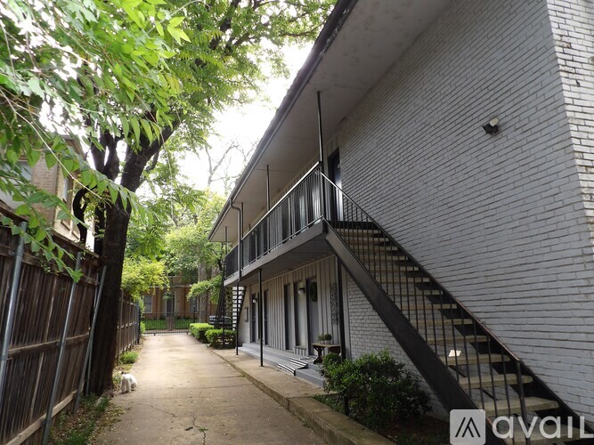 A tree-lined walkway leads to a building with a balcony.