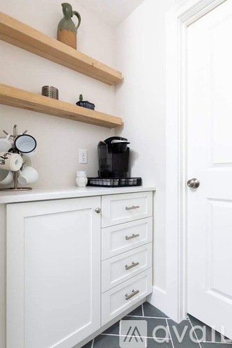 A kitchen with white cabinets and a wooden shelf above.