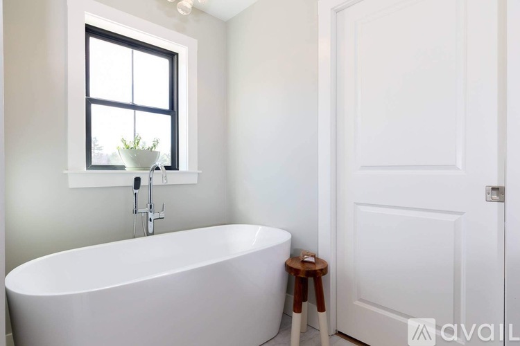 A white bathroom with a tub, window, and a plant.