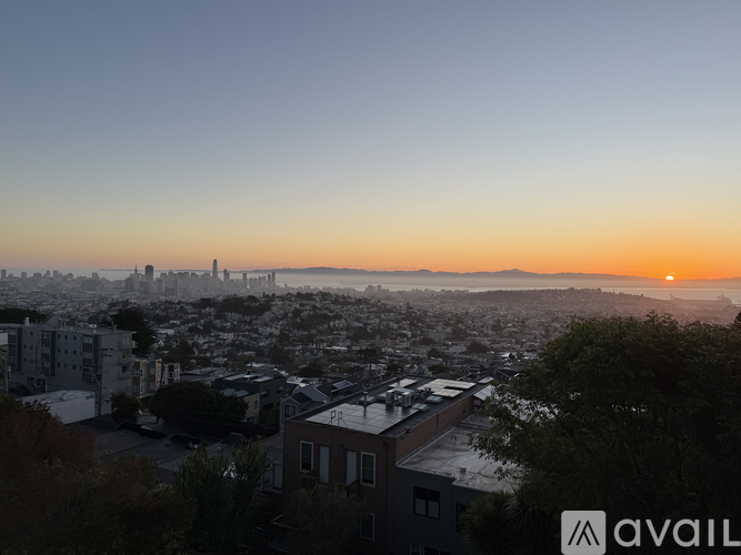A cityscape at sunset with the sun visible on the horizon.