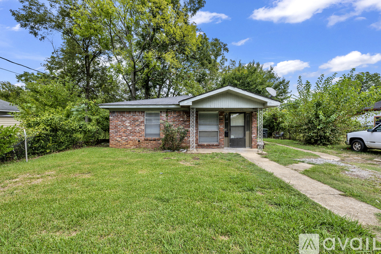 A small house with a brick exterior is surrounded by greenery and a clear sky.