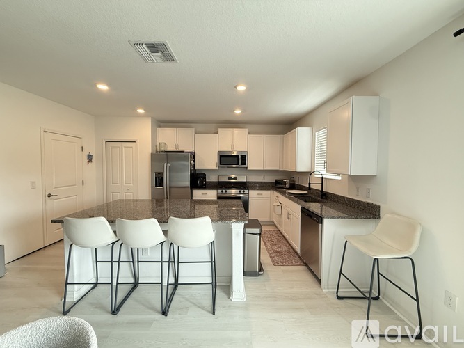 A kitchen with white chairs and a black counter.