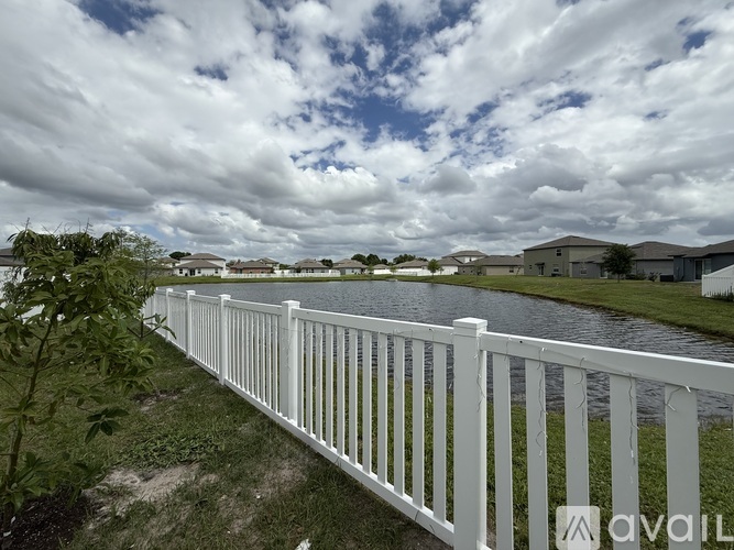A white fence runs along a grassy area next to a body of water.