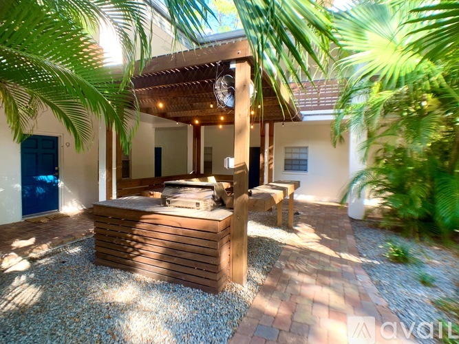 A wooden structure with a roof and a bench is surrounded by palm trees.