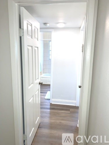 A hallway with a white door and a white bedroom in the background.