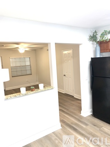 A black refrigerator is in the corner of a kitchen with a window and a door.