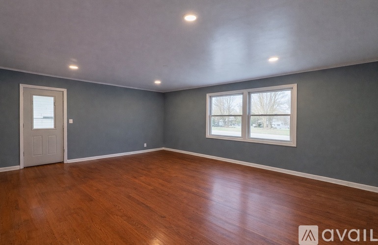 A room with wooden floors and a window showing a tree outside.