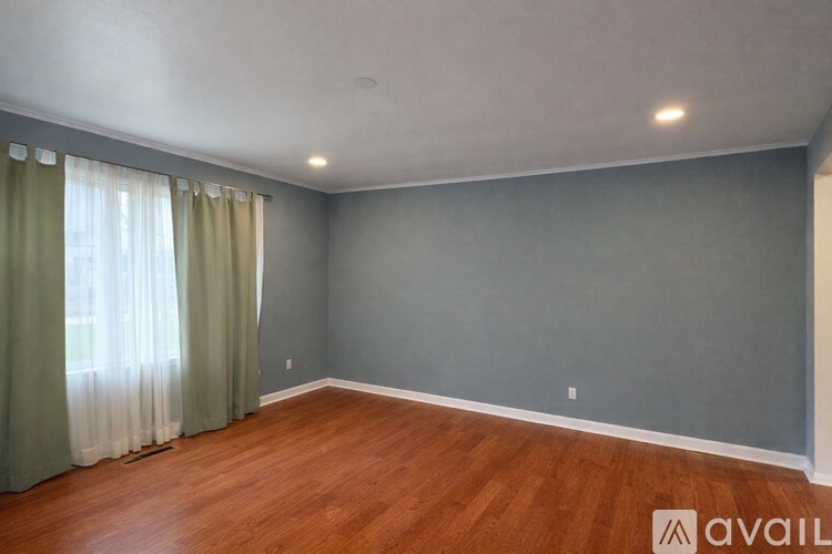 A room with wooden floors and grey walls with a window covered by curtains.
