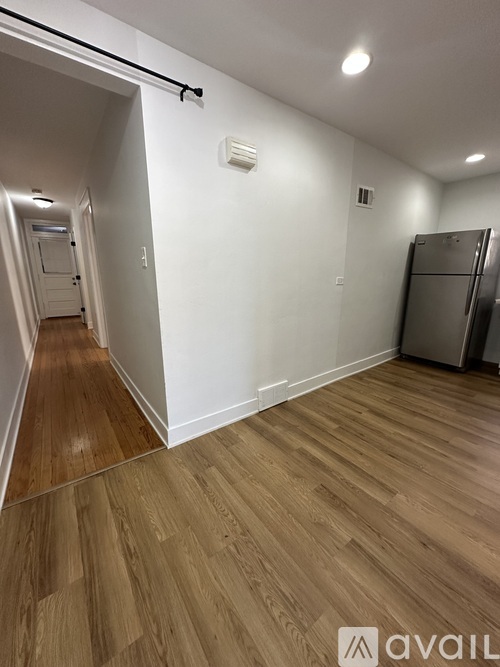 A hallway with wooden floors and white walls leading to a kitchen area.