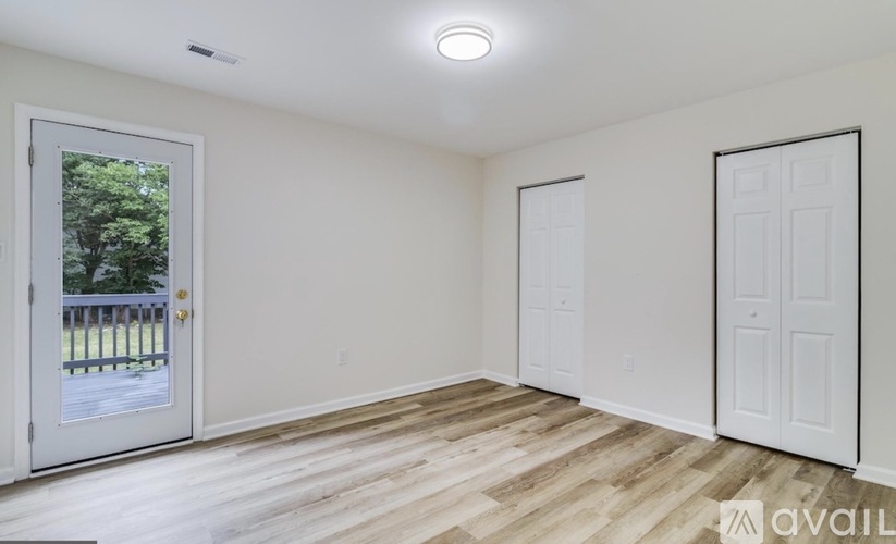 A room with a white door and a window with a view of a fence and trees.