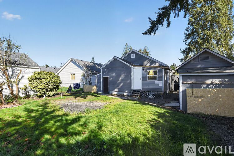 A house with a grey roof and a white door is surrounded by a grassy area.