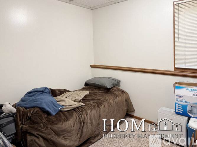 A bedroom with a bed covered in a brown blanket and a window with blinds.