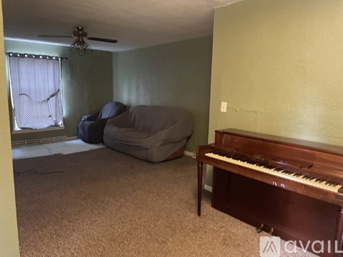 A living room with a couch, a chair, a piano, and a ceiling fan.