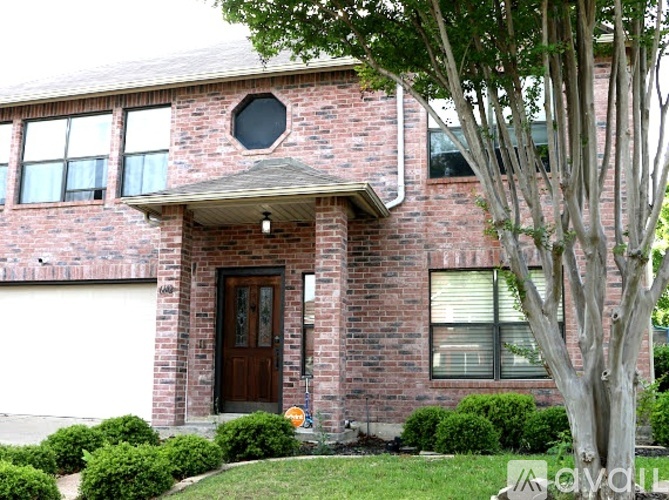 A red brick house with a brown door and a tree in front.