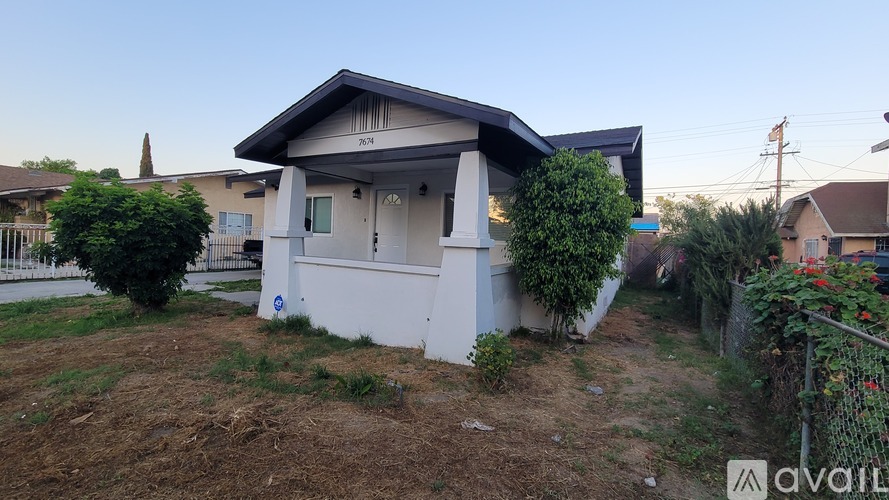 A house with a white exterior and a grey roof is surrounded by a fence and some greenery.