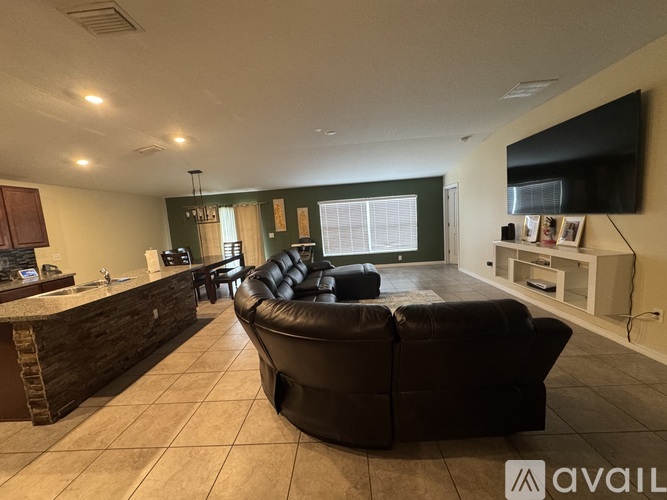 A living room with a black leather couch and a flat screen TV mounted on the wall.