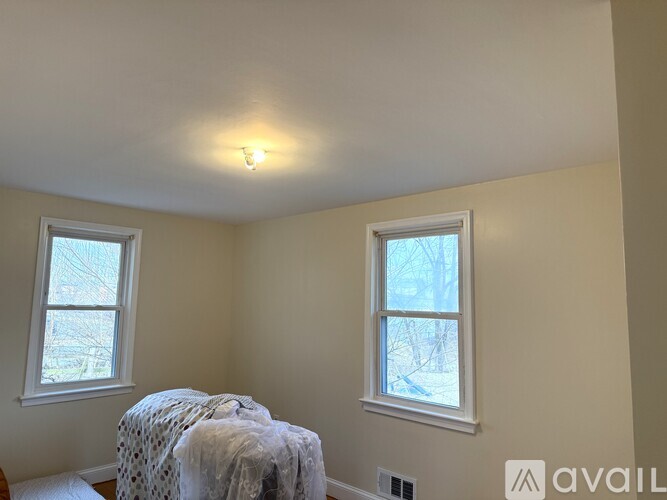 A bedroom with a bed covered in a white blanket and two windows.