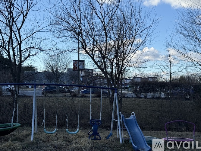 A playground with swings and a slide in the foreground and a building in the background.
